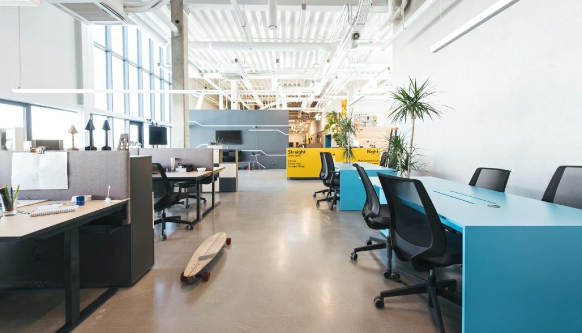 Open-plan office desking area with a blue feature table and exposed ceiling